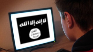 Jugendlicher sitzt am Bildschirm eines PC s mit Flagge des IS Islamischer Staat.