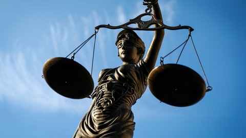Figur der Justizia hält eine Waage in der Hand. 