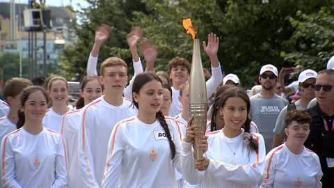 Fackelträgerinnen bringen die olympische Flamme von Weil am Rhein nach Hüningen ins Elsass
