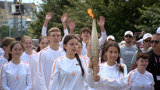 Fackelträgerinnen bringen die olympische Flamme von Weil am Rhein nach Hüningen ins Elsass