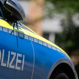 Polizeiauto mit blauem Aufdruck und gelben Streifen steht in einer Wohngegend.