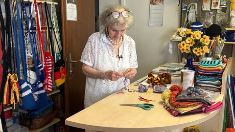 Gisela Mahler häkelt an der Ladentheke, im Hintergrund sind verschiedene Produkte ihrer Strick-Boutique in Bonndorf.