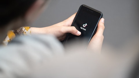 Eine Jugendliche schaut auf ein Smartphone mit angezeigtem TikTok-Logo