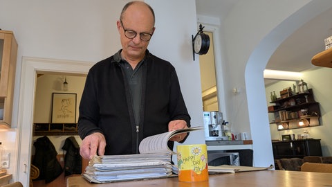 Thomas Mann blättert seine Bescheide zur Grundsteuer durch. Er freut sich über eine niedreigere Grundsteuer. Vor ihm Steht eine Tasse, auf der Happy Day steht.