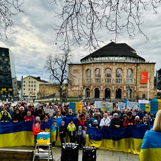 Mehrere Menschen tragen die Farben der ukrainischen Flagge am Körper oder als Fahne.