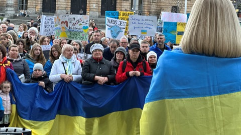 Mehrere Menschen tragen die Farben der ukrainischen Flagge am Körper oder als Fahne.