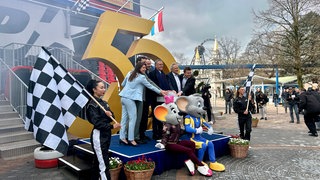 Familie Mack posiert mit den Maskottchen des Europa-Parks vor einer goldenen 50.