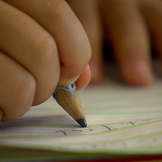Finger, die einen Bleistift halten und in einem Linienheft Schreiben lernen