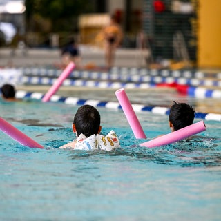 Kinder üben im Schwimmunterrticht im Hallenbad mit sogenannten Schwimmnudeln