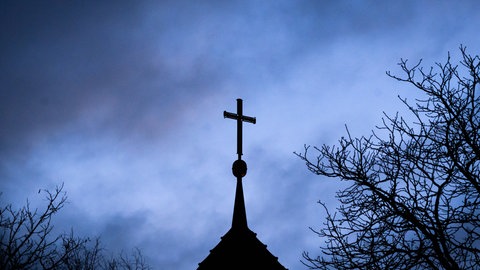Die Spitze eines Kirchturms mit einem Kreuz vor einem gewittrigen Hintergrund. 