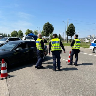 Drei Polizisten kontrollieren einen PKW, der am Straßenrand parkt