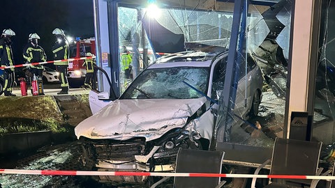 Ein weißes Auto hat bei einem Unfall die Scheibe eines Autohauses durchbrochen.
