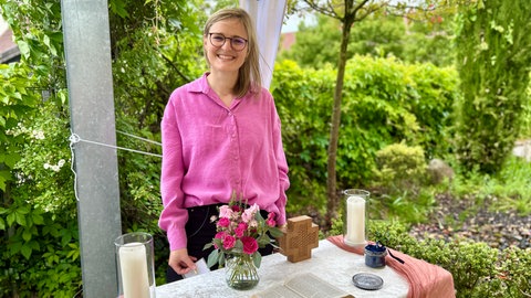 Pfarrerin Nadine Kempf steht vor einem Altar, der feierlich mit Blumen und Kerzen geschmückt ist.