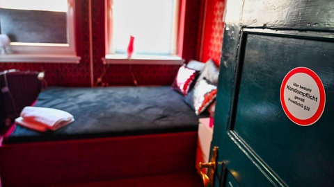 Die Tür steht offen zu einem Zimmer mit einem Bett, auf der Tür steht "Hier besteht Kondompflicht"
