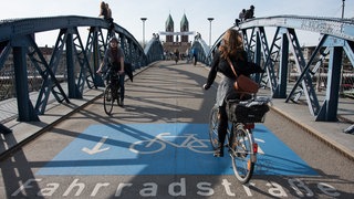 Man sieht die Blaue Brücke in Freiburg, die Stühlinger Kirche und Fahrradfahrende auf der Brücke.