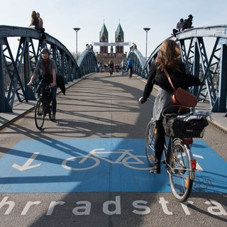 Man sieht die Blaue Brücke in Freiburg, die Stühlinger Kirche und Fahrradfahrende auf der Brücke.