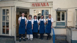 Ein fünfköpfiges Küchen-Team steht vor einem Gebäude.