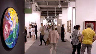 Viele Menschen schauen sich bunte Bilder bei der Art Basel in einem Ausstellungsraum an.