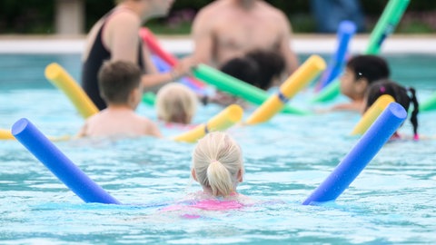 Bei einer Schwimmstunde lernen Kinder Schwimmen mit einer Schwimmnudel.