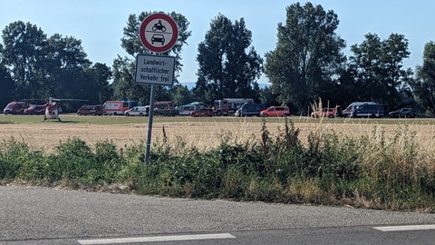Ein Hubschrauber und viele Einsatzfahrzeuge stehen auf einer Straße in der Nähe des Baggersees.