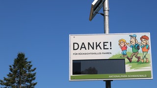 Auf einer Tafel steht "Danke für rücksichtsvolles Fahren". Drei gezeichnete Wanderer sind zu sehen und in der Mitte eine digitale Anzeige. Dort kann man in Echtzeit sehen, wie laut es gerade ist.