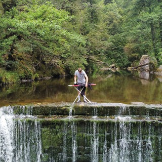 Extrembügler steht über einem Wasserfall und bügelt.
