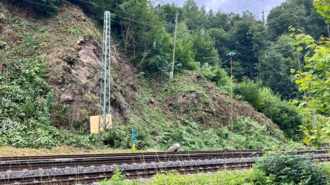 Man sieht ein Felsstück, das auf das Gleis gefallen ist. Das Holzbrett soll den Strommasten schützen.