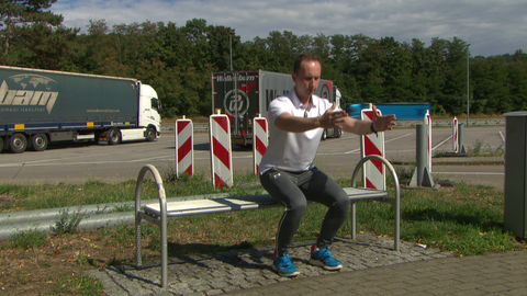Ein Physiotherapeut zeigt an einer Raststätte eine Kniebeuge. 