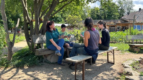 Eine Gruppe von Menschen spielt in einem Garten ein Kartenspiel. Es ist der inklusive Gemeinschaftsgarten in Freiburg, in dem für alle Platz ist.