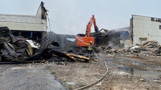 Die Feuerwehr löscht weiterhin eine vom Brand betroffene Halle. Teile müssen eingerissen werden.