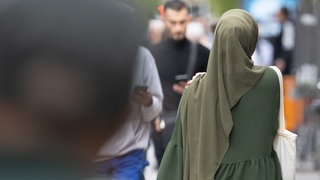 Eine Frau mit Kopftuch und Einkaufstasche in einer Fußgängerzone.