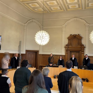 Das Gericht betritt den am ersten Prozesstag den Gerichtssaal. Ein 21-Jähriger ist angeklagt, seine Mutter ermordet zu haben. 