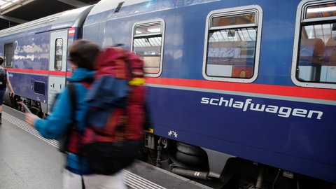 Ein Reisender mit einem Rucksack läuft vor einem Nachtzugwagen vorbei, auf dem das Wort Schlafwagen steht