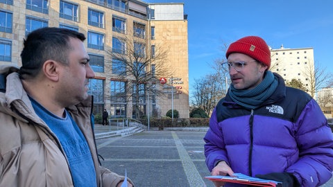 Der Freiburger Bundestagsabgeordnete Vinzenz Glaser von der Partei Die Linke spricht mit einem Mann vor dem Jobcenter in Freiburg.