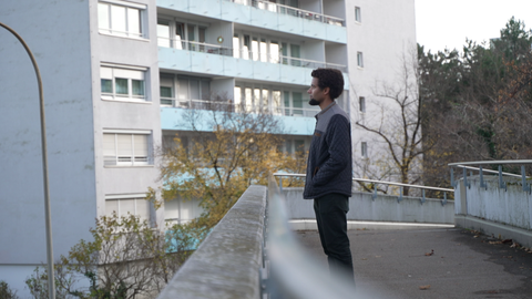 Junger Mann steht an einer Brücke und schaut in die Weite.