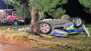 Ein verbeultes Polizeiauto liegt auf dem Dach neben einem Baum. Bei dem Unfall ist ein Polizeibeamter ums Leben gekommen, ein zweiter wurde mit einem Rettungshubschrauber in eine Klinik geflogen. 