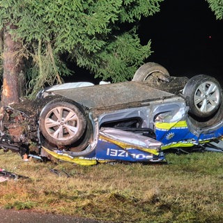 Ein verbeultes Polizeiauto liegt auf dem Dach neben einem Baum. Bei dem Unfall ist ein Polizeibeamter ums Leben gekommen, ein zweiter wurde mit einem Rettungshubschrauber in eine Klinik geflogen. 