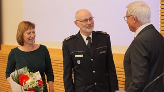 Ein Mann in Uniform lächelt und bekommt Blumen.
