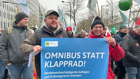 Drei Männer stehen mit einem Plakat auf einer Demo.