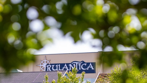 Zwischen Blättern lugt ein Stück einer Gebäudefassade hervor mit der Aufschrift "Rulantica".