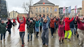 Die Teilnehmerinnen und Teilnehmer beim Tanzflashmob "One Billion Rising" gegen Gewalt an Frauen recken die Arme in den Himmel auf dem Platz der alte Synagoge in Freiburg.