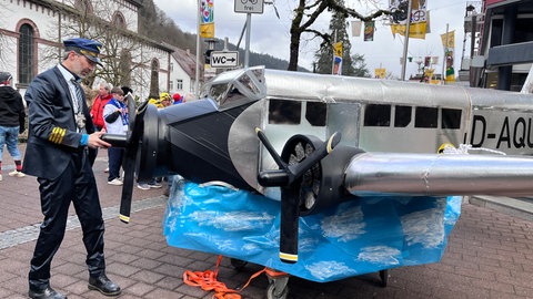 Der Pilot dieses Holzzubers in Flugzeugform richtet vor dem Start noch den Propeller seines Gefährts.