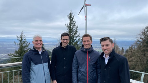 Vier Männer stehen vor einem Windrad.