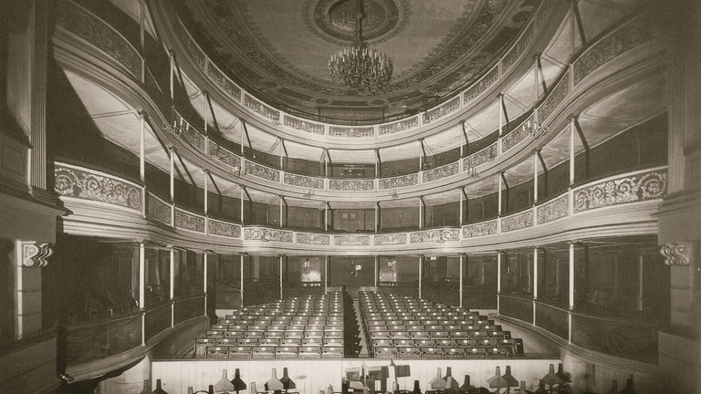 Ein Zuschauerraum mit Bühne und Kronleuchter, historische Aufnahme