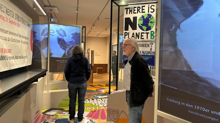 Auch über die neuere Geschichte Freiburgs informiert das Augustinermuseum - etwa die Hausbesetzungen in den 1070ern oder die Klimastreiks der vergangenen Jahre. Ein Mann betrachtet entsprechende Plakate. Auch der Boden ist mit Protestslogans bedruckt.