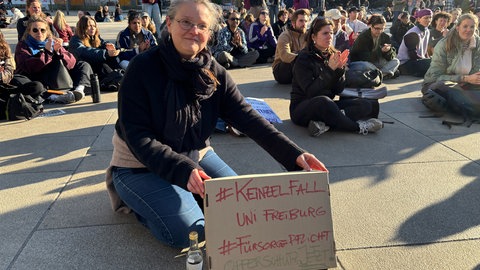 Eine Demonstrantin mit einem Plakat "#Keinzelfall Uni Freiburg #Fürsorgepflicht Opferschutz jetzt!"