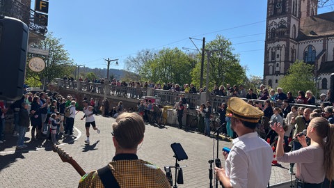 Viele Menschen in Sportklamotten laufen durch die Straßen Freiburg. Am Straßenrand stehen Bands und viele Zuschauer. Viele von ihnen halte Pappschilder hoch.