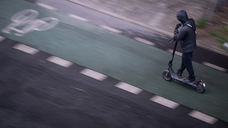 Ein Mann fährt mit einem E-Scooter auf einem Fahrradweg. 