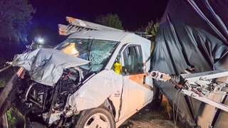 Ein Auto mit einem Anhänger stehen nach einem Unfall zerstört auf einer Straße.
