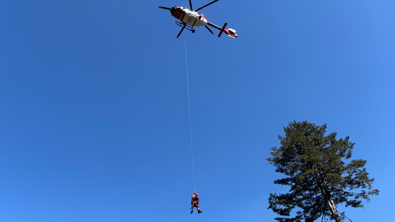 Zwei Rettungskräfte von DRF Luftrettung und Bergwacht werden an der Seilwinde in den Rettungshubschrauber gezogen.